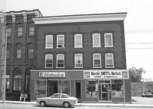 L’épicerie boucherie Swett Bros. est un client régulier de Pine Tree Farm. Le commerce de la rue Principale s’y procure une grande quantité de viandes de mouton et d’agneau, destinées à la population anglaise de la ville. L'édifice, tel qu'il apparaît en 1978. (Fonds Patrimoine architectural, inventaire et analyse, SHHY)